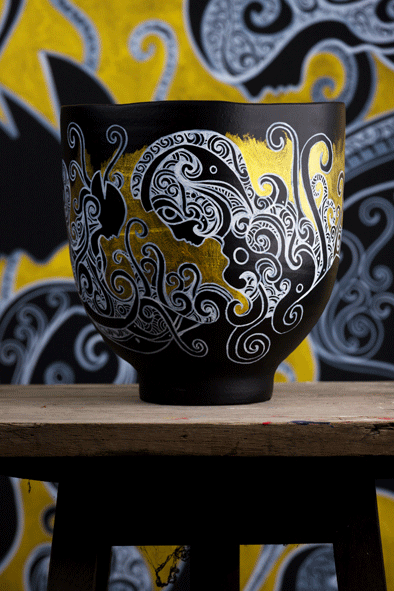 A beautiful black vases with a beautiful hand drawn and painted artwork on it by artist Kenneth Kenisman made with a white acrylic markers and gold paint. The artwork shows an abstract landscape with sea waves and curls and beautiful woman figures wearing an ancient helmet.